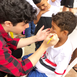 Foto de voluntário com criança fazendo pintura facial.
