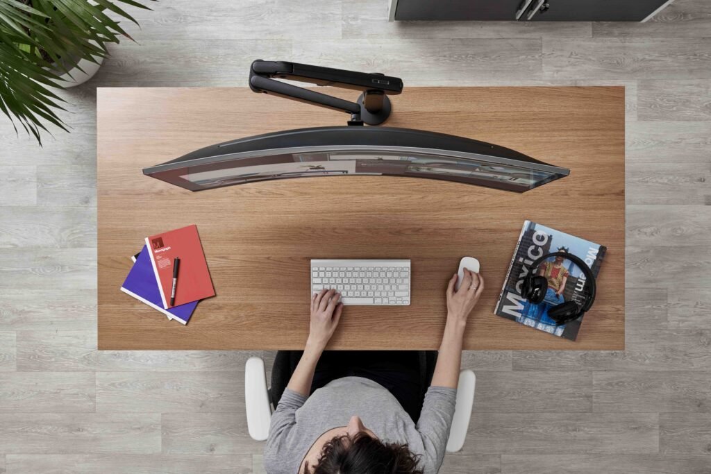 Imagem vista de cima de uma mesa com uma pessoa utilizando monitor wide screen e suporte Ollin na cor preta