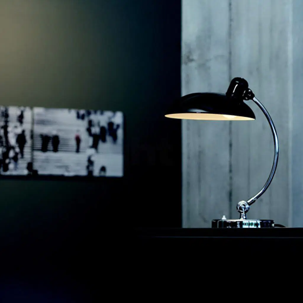 Luminária Kaiser preta sobre mesa em ambiente com pouca luz.