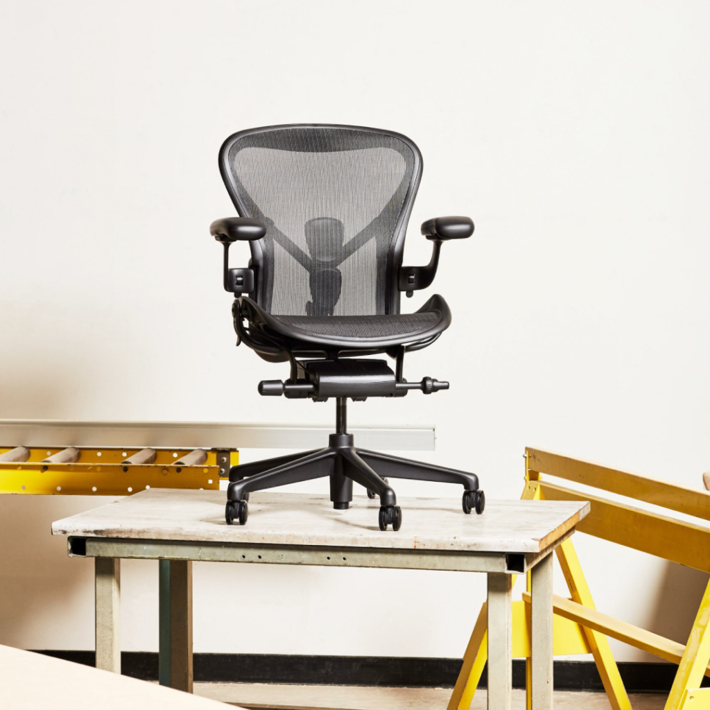 Uma cadeira Aeron na cadeira Onyx, sobre uma mesa de madeira, em ambiente de oficina.